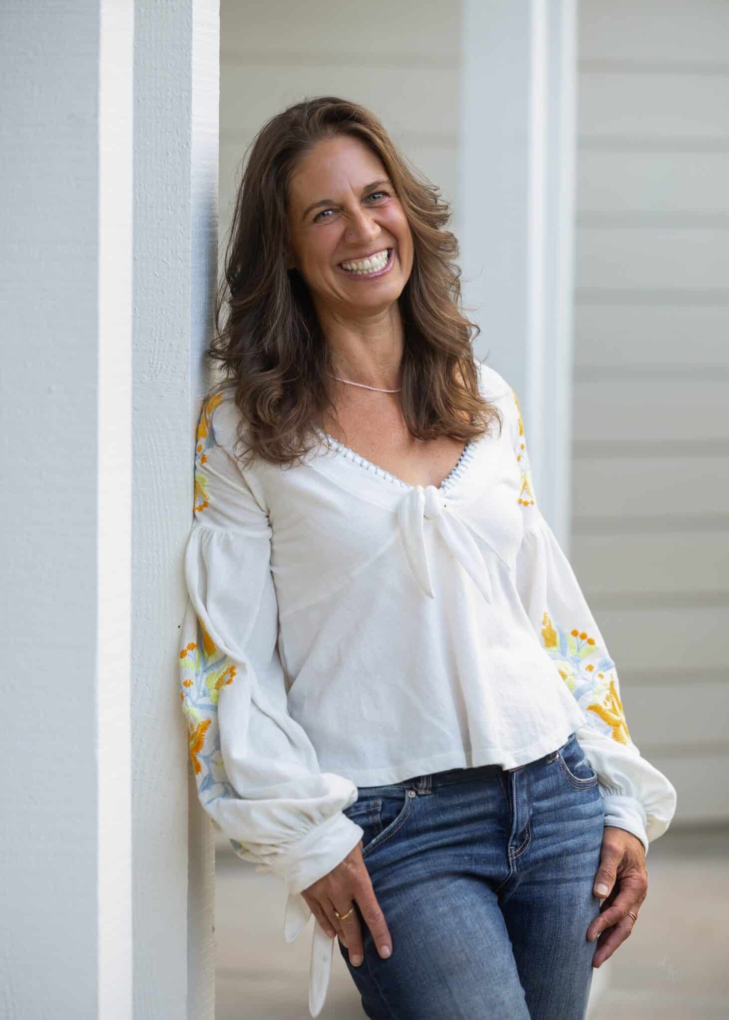 Jennifer Jo, smiling and leaning against a porch column